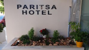 A sign for the Paritsa Hotel with a rock garden and potted plants in front.