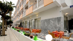 A hotel exterior with outdoor seating, a planter with plants, and a marble wall. - Paritsa Hotel (Kos)