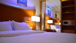 A hotel room with a large bed, two bedside lamps, a mirror, and a wooden headboard. - Belle Vue Hotel (Amman)