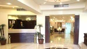 A hotel lobby with a reception desk, potted plants, a geometric floor design, and a staircase leading to another area. - Belle Vue Hotel (Amman)