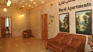 A lobby with a brown leather sofa, a wooden bench, and a wall with 'Royal Apartments' signage. - Belle Vue Hotel (Amman)