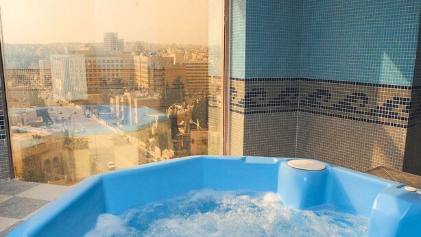 A hot tub with a city view through a window. - Belle Vue Hotel (Amman)