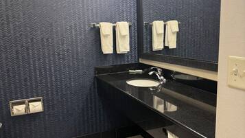 Un baño con piso a cuadros blanco y negro, un lavamanos y dos toallas colgadas en un perchero.