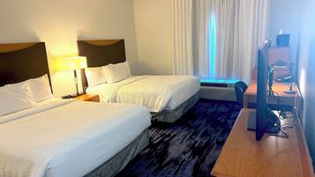 Habitación de hotel con dos camas, un escritorio con computadora y una ventana con cortinas.