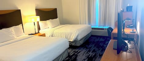 A hotel room with two beds, a desk with a computer, and a window with curtains.