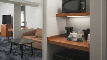 A hotel room with a sofa, a small table, a microwave, a coffee maker, and a refrigerator.
