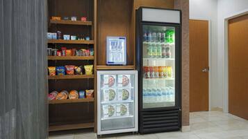 Zona de máquinas expendedoras con refrigerios, un expositor refrigerado y un enfriador de bebidas.