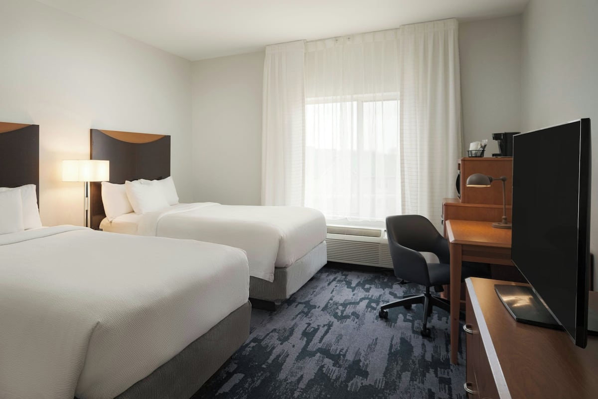 A hotel room with two beds, a desk with a computer, a chair, and a large TV.