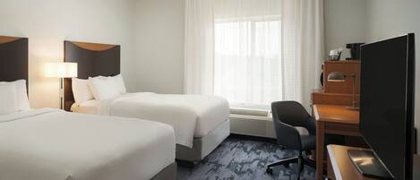 A hotel room with two beds, a desk with a computer, a chair, and a large TV.