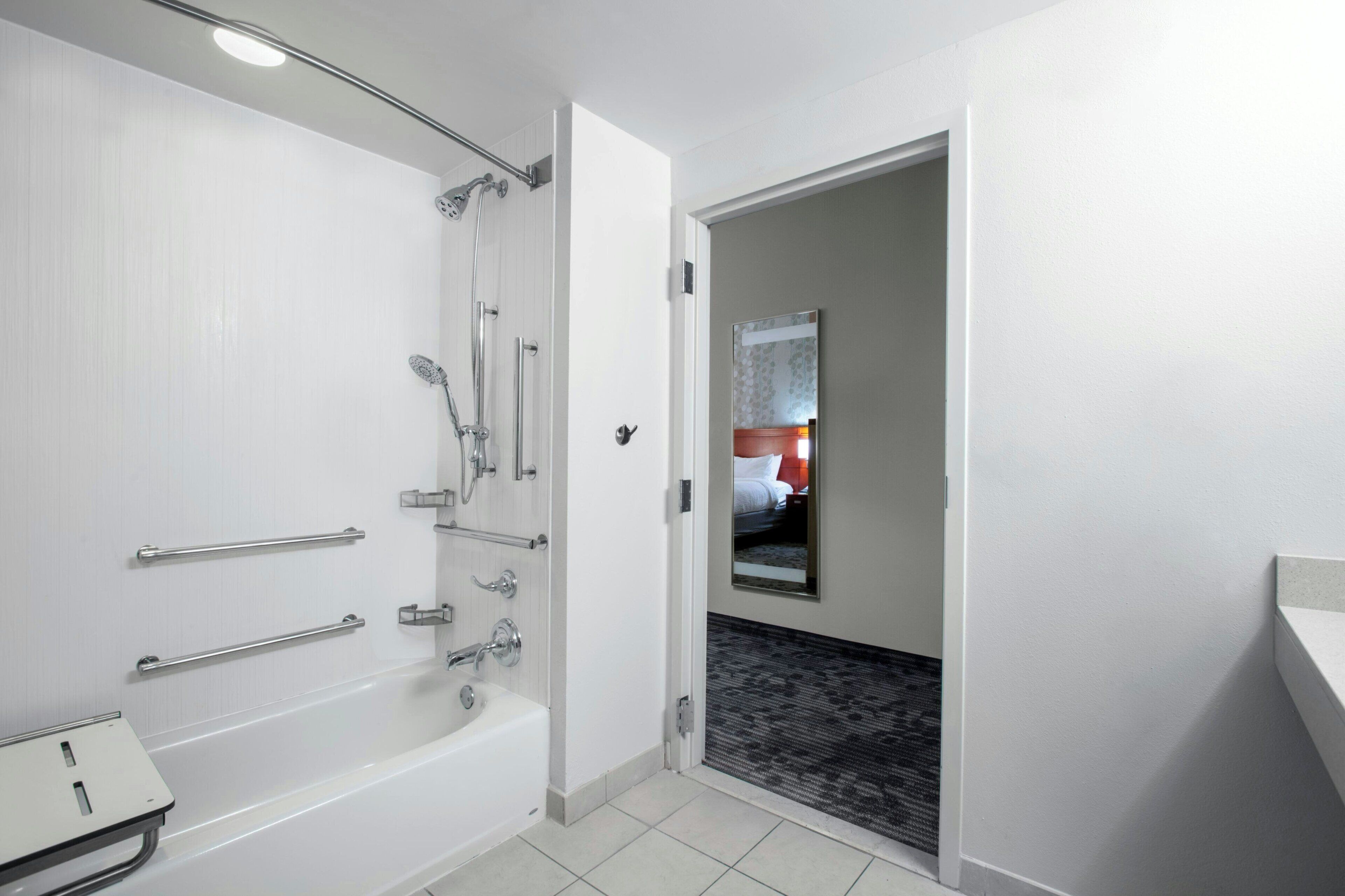 A modern bathroom with a bathtub, shower, and handrails.
