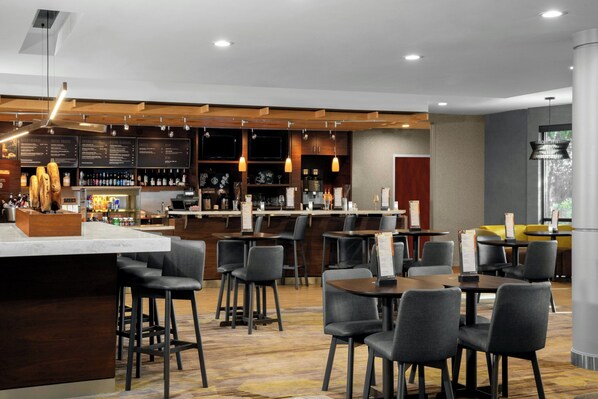 Un restaurante moderno con zona de bar, diversas opciones de asientos que incluyen taburetes y mesas, y varios menús a la vista.