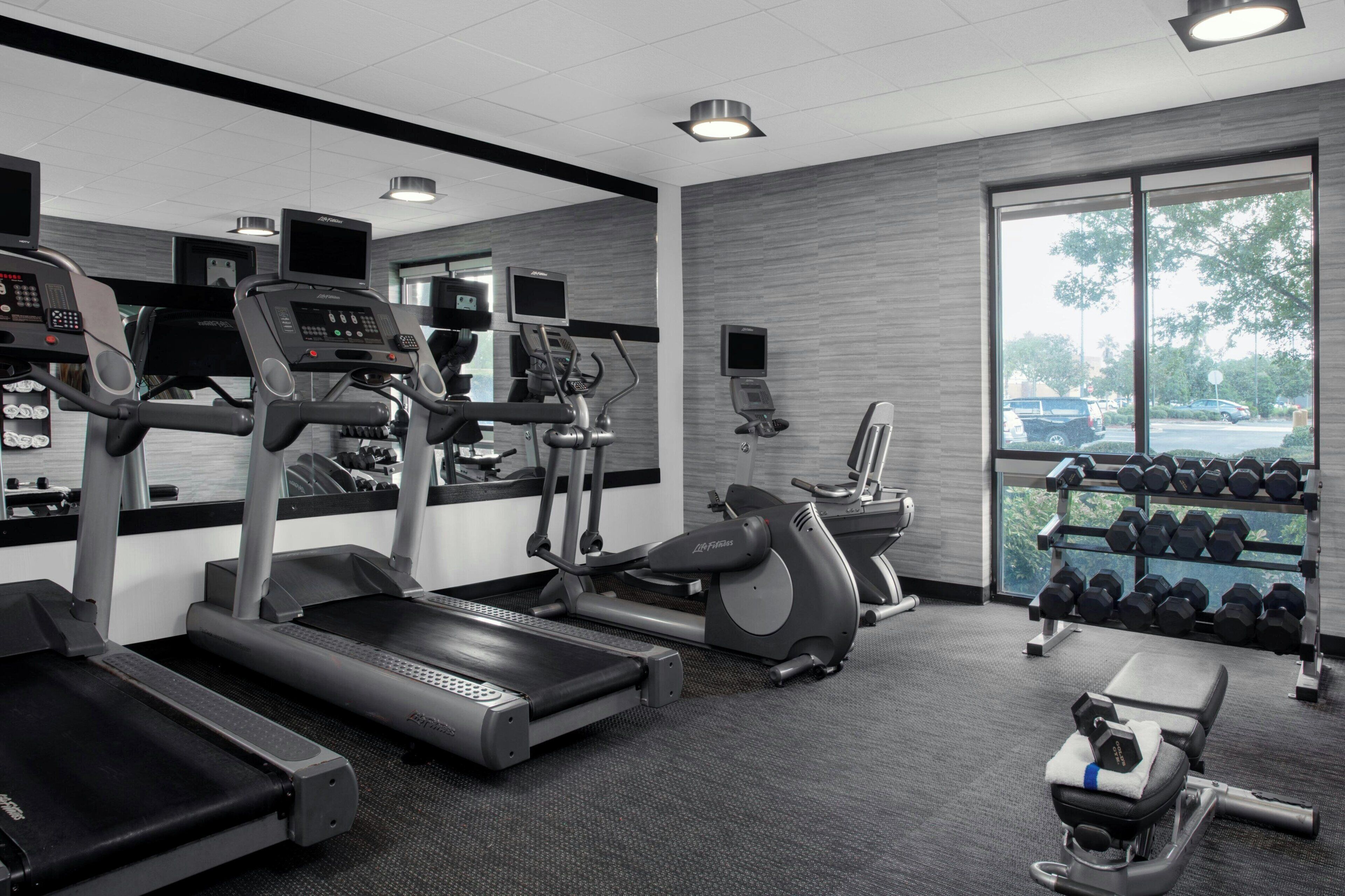 A gym with treadmills, elliptical machines, a stationary bike, and a bench.