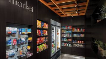 A grocery store with shelves stocked with snacks and beverages, a refrigerated section, and a wooden ceiling.