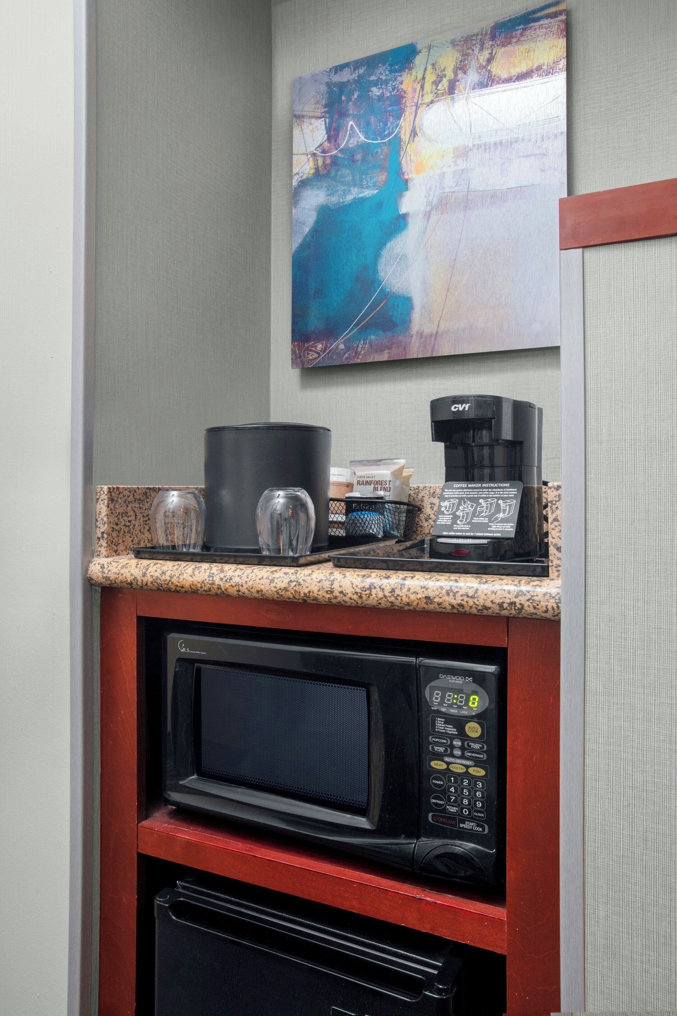 A kitchenette with a coffee maker, microwave, and glassware on a granite countertop.