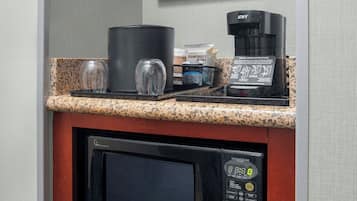 A kitchenette with a coffee maker, microwave, and glassware on a granite countertop.