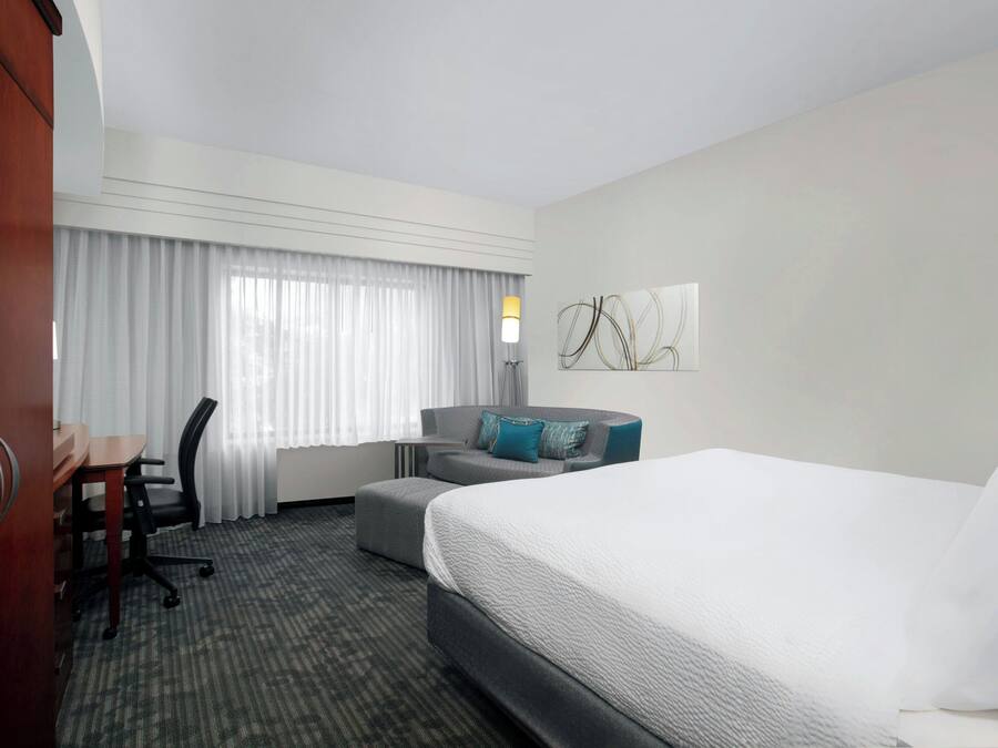 A hotel room with a bed, a desk, a chair, and a sofa.