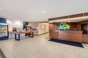 A modern reception area with a wooden reception desk, a coffee station, and a refrigerator displaying beverages.