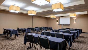 Un salón de conferencias con mesas y sillas, una pantalla de proyector y luces en el techo.
