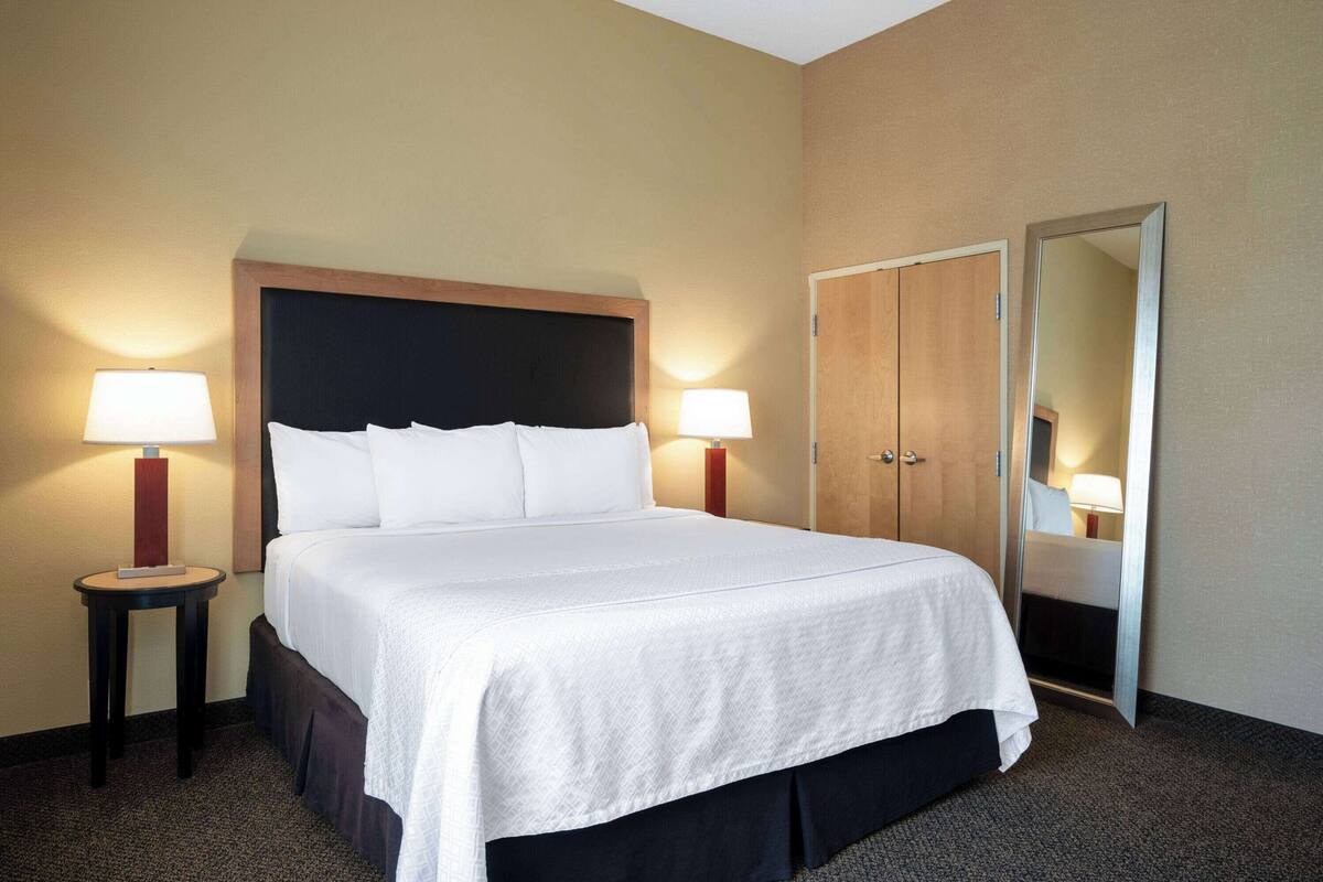 Une chambre d’hôtel avec un grand lit, deux tables de chevet avec des lampes, une armoire et un miroir.