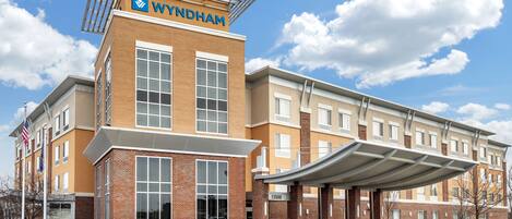 Un hotel Wyndham con un diseño moderno, que cuenta con una entrada destacada y un área de estar al aire libre cubierta.