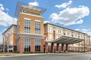 Un hotel Wyndham con un diseño moderno, que cuenta con una entrada destacada y un área de estar al aire libre cubierta.