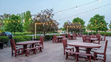 An outdoor patio area with wooden tables and chairs, string lights, and trees.