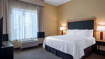 A hotel room with a large bed, two bedside lamps, a flat-screen TV, a heater, and a window with sheer curtains.
