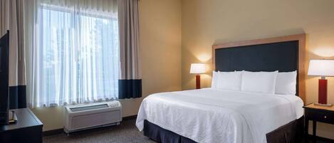 Een hotelkamer met een groot bed, twee bedlampen, een flatscreen televisie, een verwarming en een raam met dunne gordijnen.