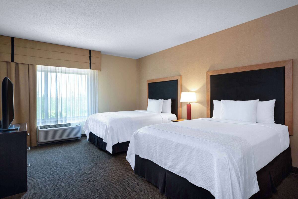 Une chambre d’hôtel avec deux lits, une télévision, un bureau et une fenêtre avec des rideaux.