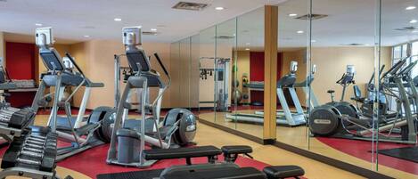 Een fitnessruimte met loopbanden, elliptische trainers en gewichtbanken.