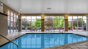 Ein Hallenbad mit großen Glaswänden, Fliesenboden und Blick auf Sitzgelegenheiten und Bäume im Freien.