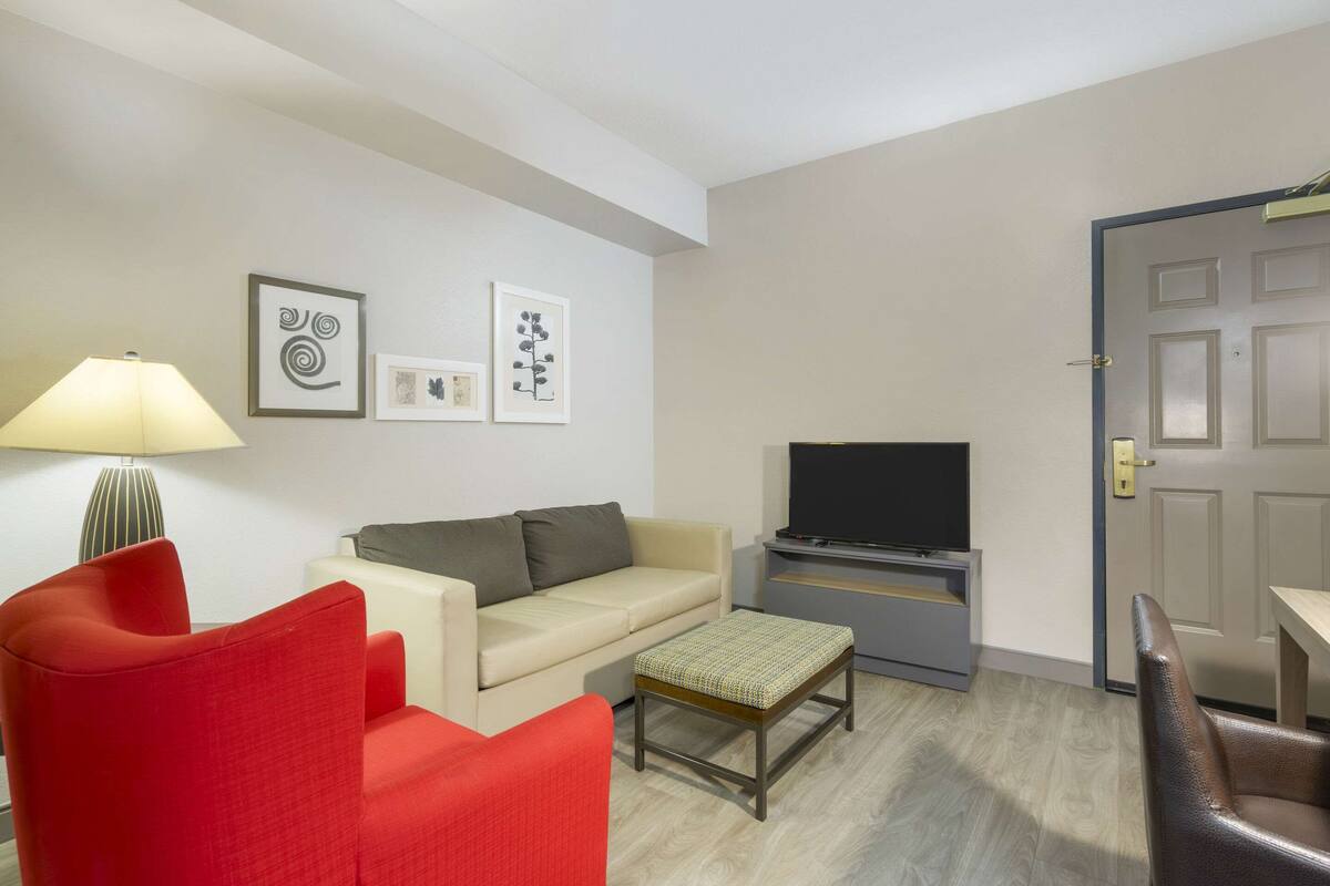 A living room with a sofa, a red armchair, a television, and a lamp.