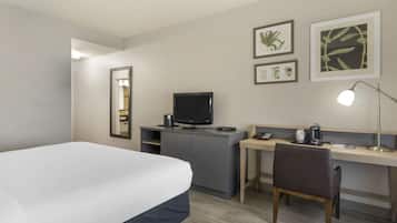 Una habitación de hotel con una cama, un escritorio con computadora, un espejo y arte botánico enmarcado en la pared.