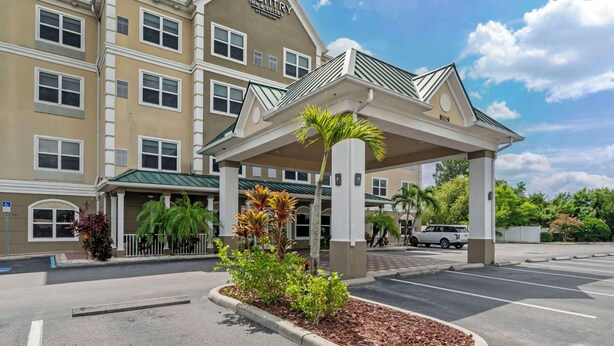 Un bâtiment Country Inn & Suites doté d’une entrée couverte, de palmiers et d’un parking.