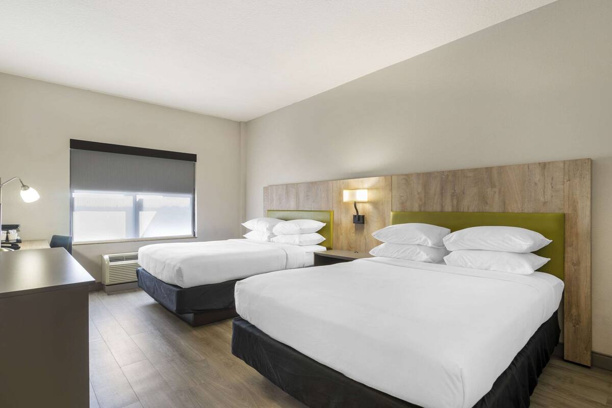 A hotel room with two beds, a desk, a lamp, and a window with blinds.