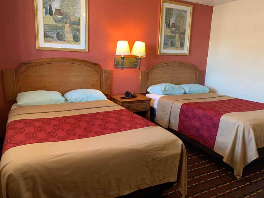 Habitación de hotel con dos camas, cada una con cabecero de madera y edredón estampado. Dos lámparas de pared a cada lado de las camas y dos cuadros enmarcados sobre ellas.