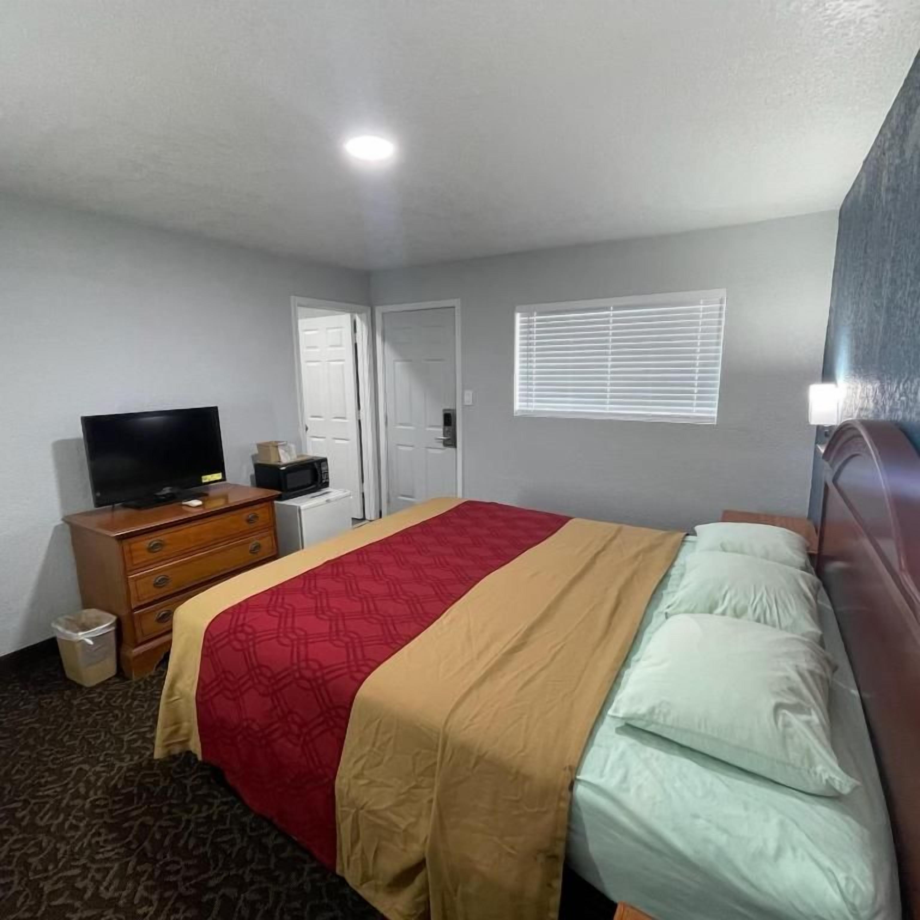 A hotel room with a bed, a television, a dresser, and a window with blinds.