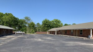 A parking lot with two brick buildings, one with a covered porch. - Budget Inn Madill (Madill)
