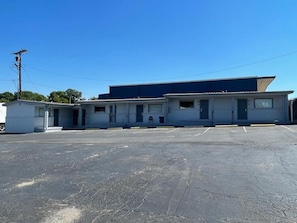 A row of single-story buildings with a parking lot in front. - Budget Inn Madill (Madill)