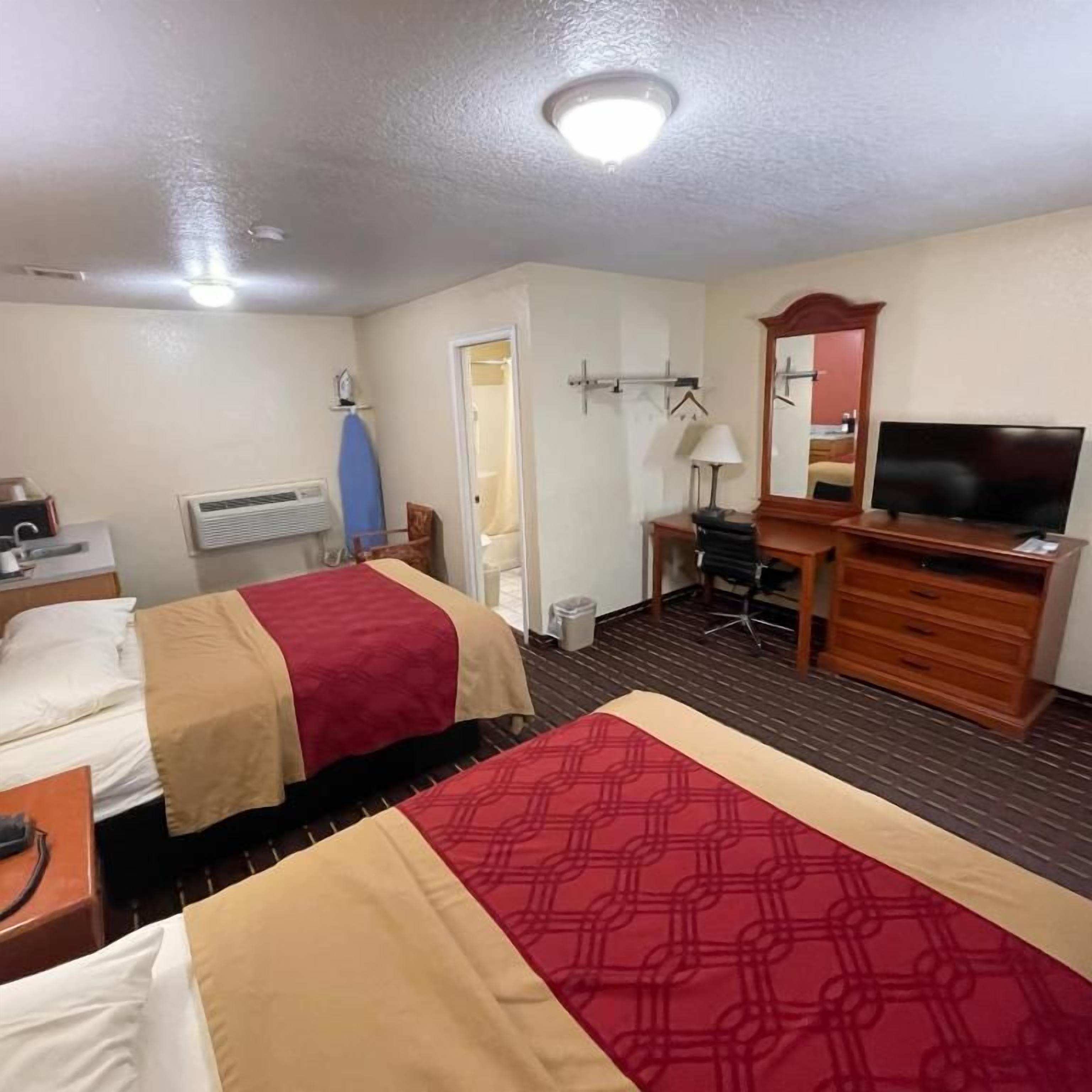 A hotel room with two beds, a desk with a chair, a television, and a mirror.