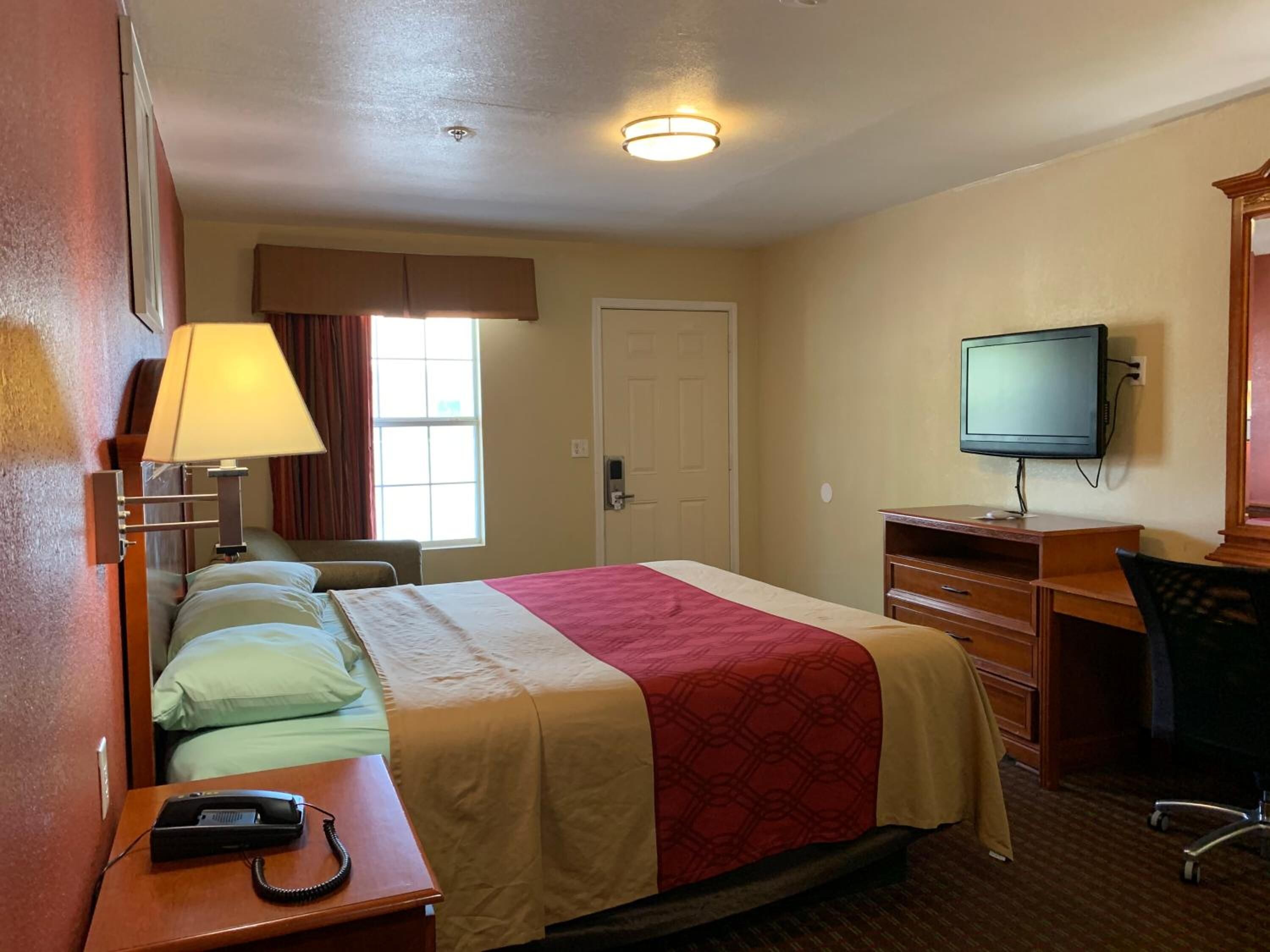 A hotel room with a bed, a desk with a telephone, a television, and a chair.