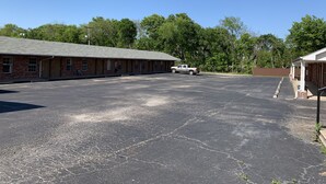 A motel with a parking lot, a truck, and a covered area with a brick building. - Budget Inn Madill (Madill)