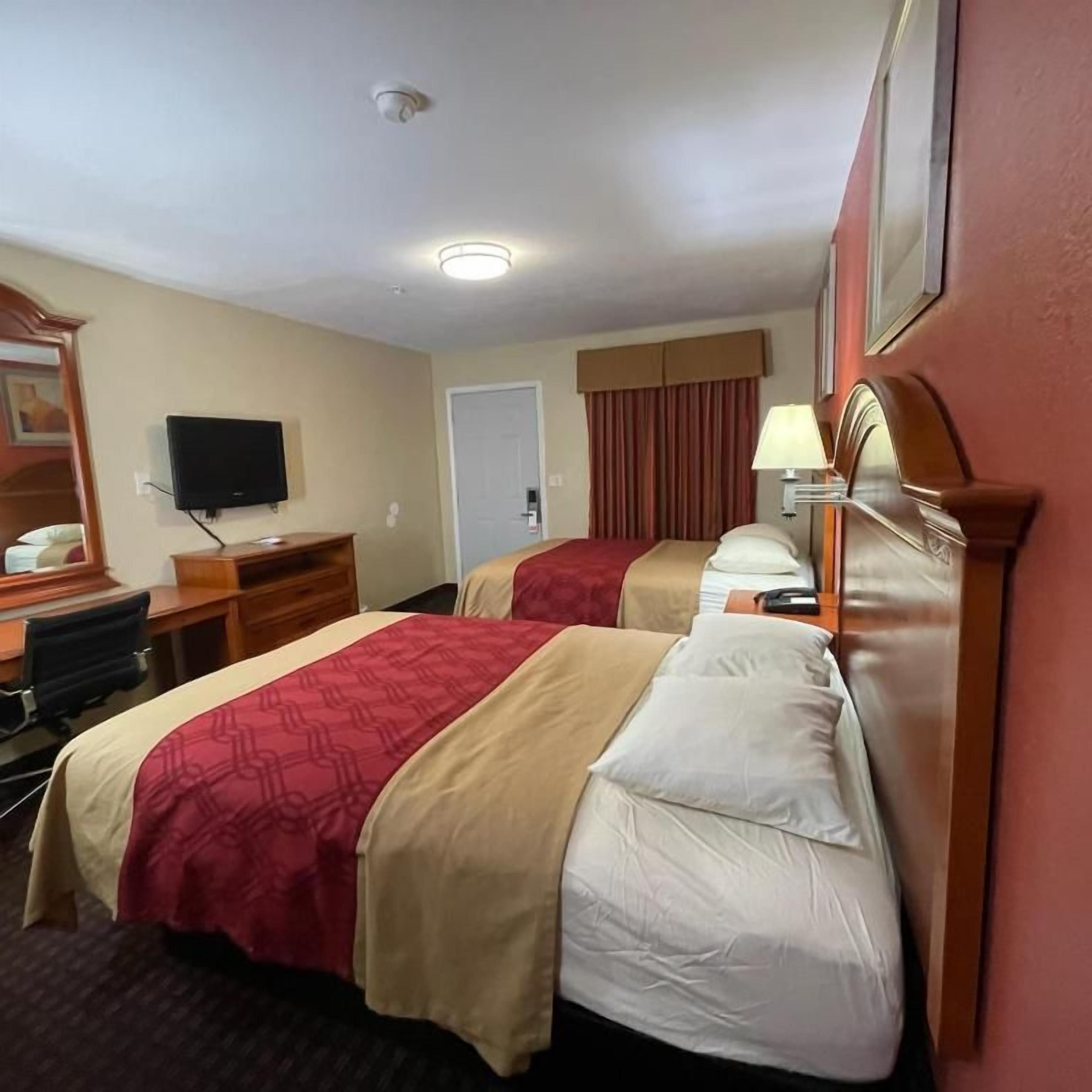 Habitación de hotel con dos camas, un escritorio, un televisor y una lámpara.