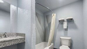 A bathroom with a granite countertop sink, a bathtub with a shower curtain, and a toilet. - Budget Inn Madill (Madill)