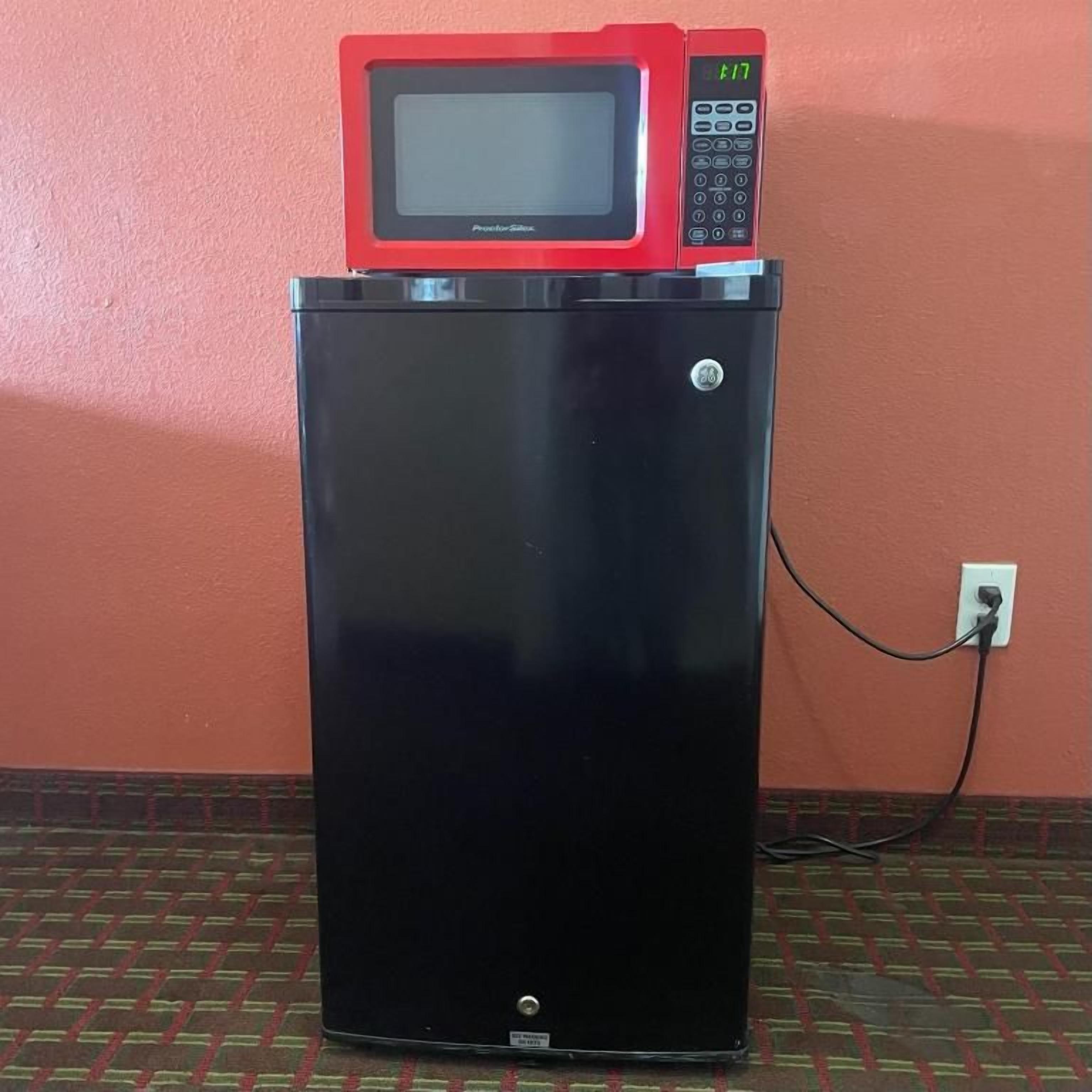 Un refrigerador negro con un microondas rojo encima, conectado a un enchufe en un piso con diseño.