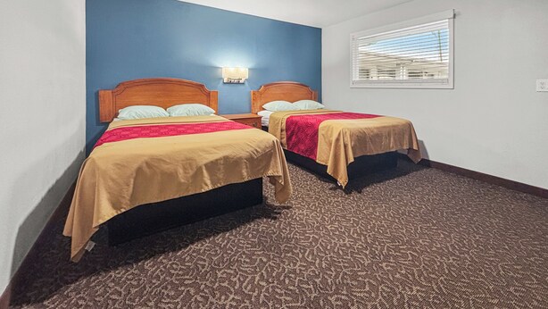 A hotel room with two beds, a blue accent wall, a window with blinds, and a carpeted floor. - Budget Inn Madill (Madill)