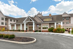 A multi-story building with a covered entrance, a parking lot, and landscaped areas.