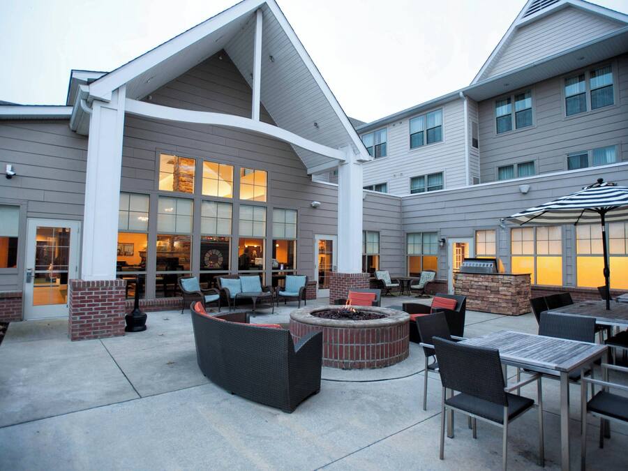 An outdoor patio area with seating, a fire pit, and a view of the building's interior.
