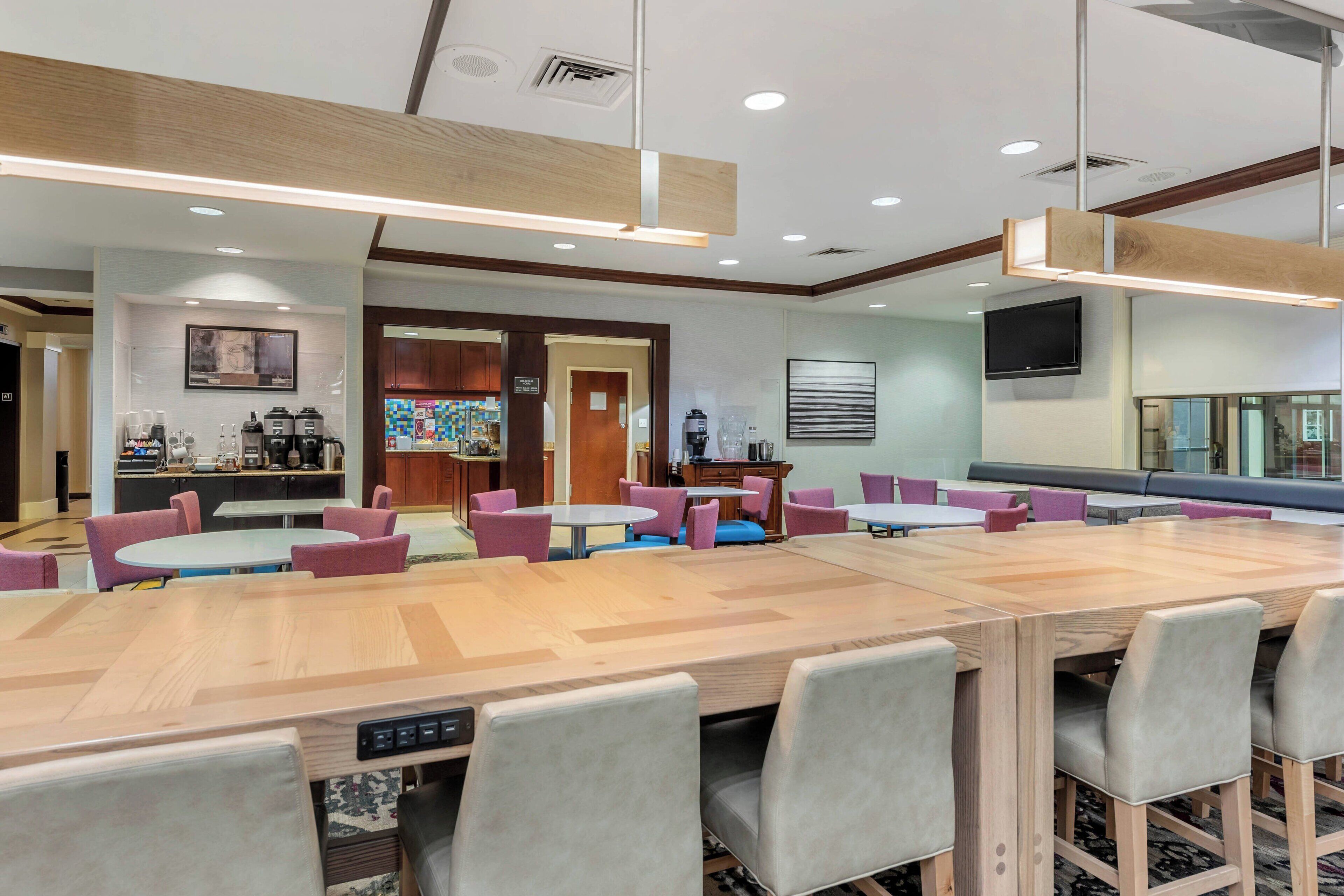 A modern conference room with a large wooden table, multiple chairs, and a television mounted on the wall.