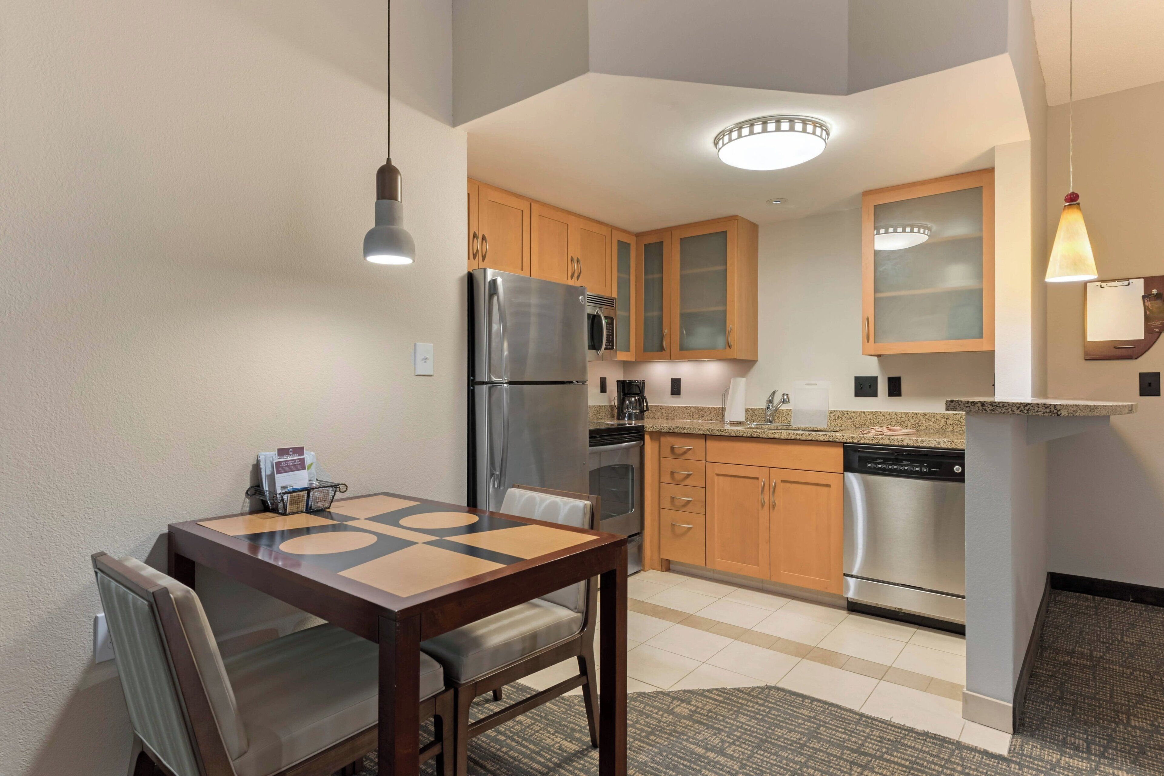 A compact kitchen with wooden cabinets, a stainless steel refrigerator, a microwave, and a dishwasher.